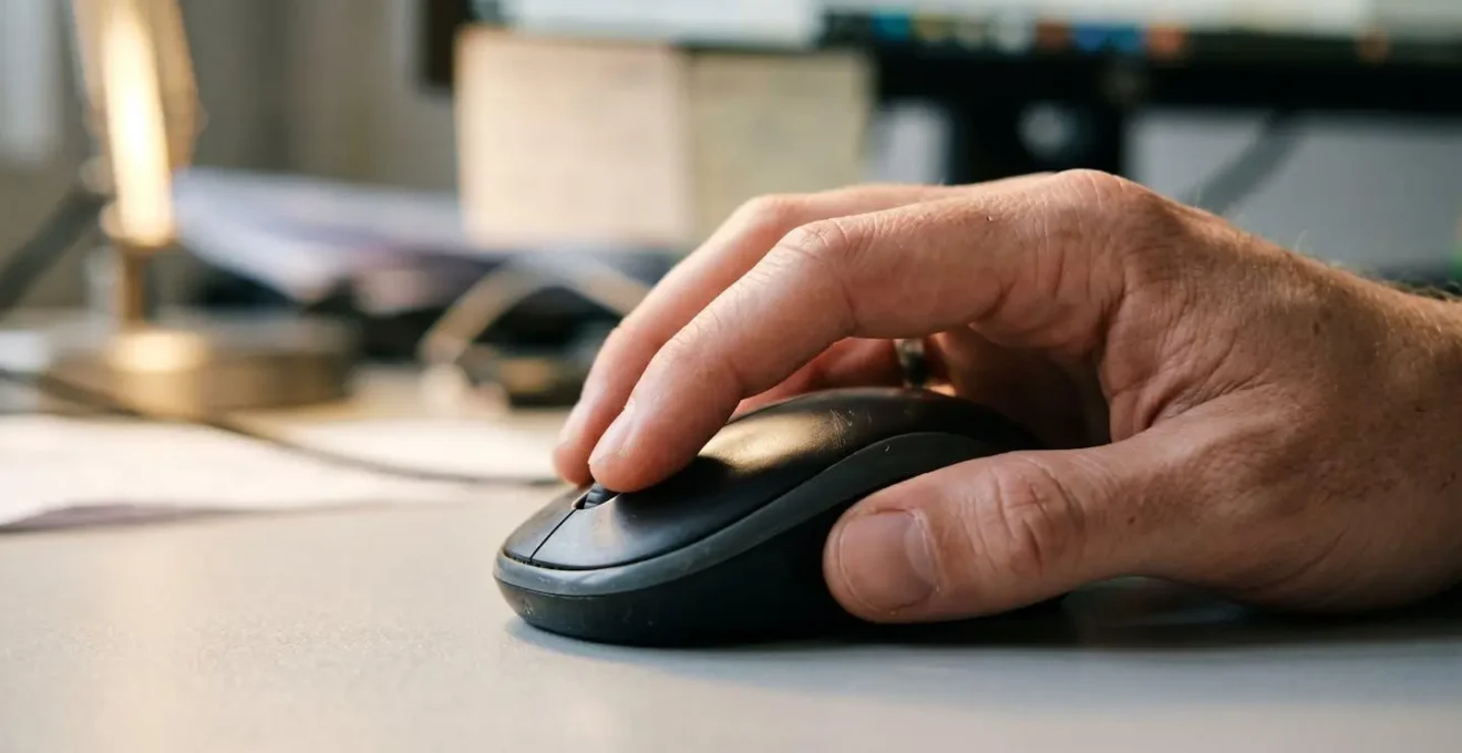 Extreme close-up of a hand positioned on a modern wireless computer mouse with fingers resting naturally on the buttons, clean white desk surface blurred in background